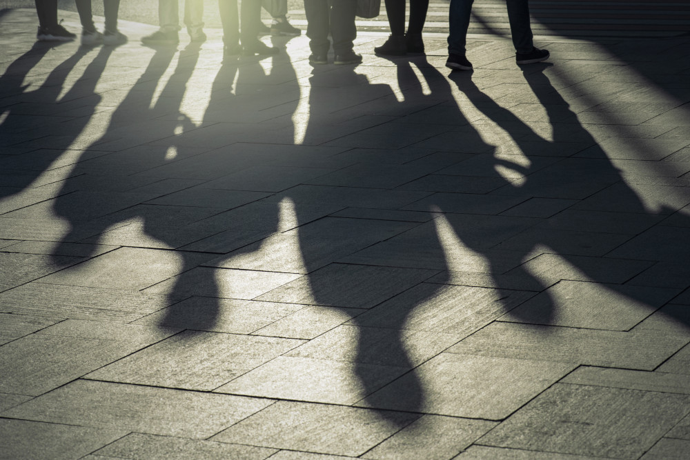 Shadows and silhouettes of people on a city sidewalk during sunset.