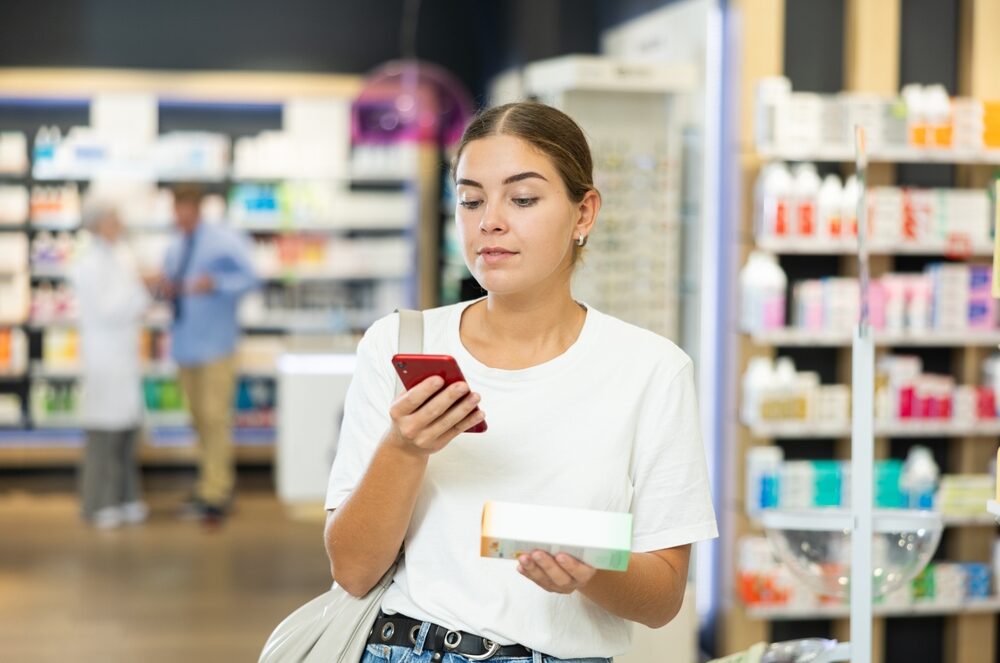 Woman using her smartphone to scan a QR code on a beauty product in the cosmetics aisle.