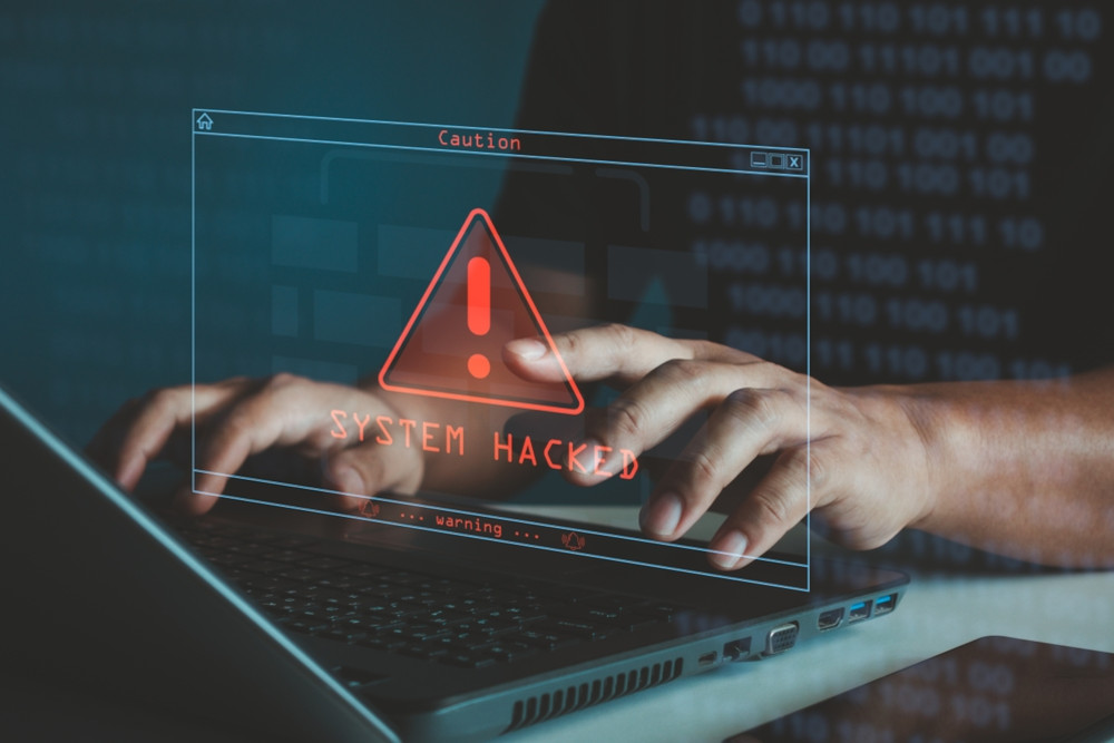 Man typing on a laptop with an overlay displaying a 'system hacked' message.