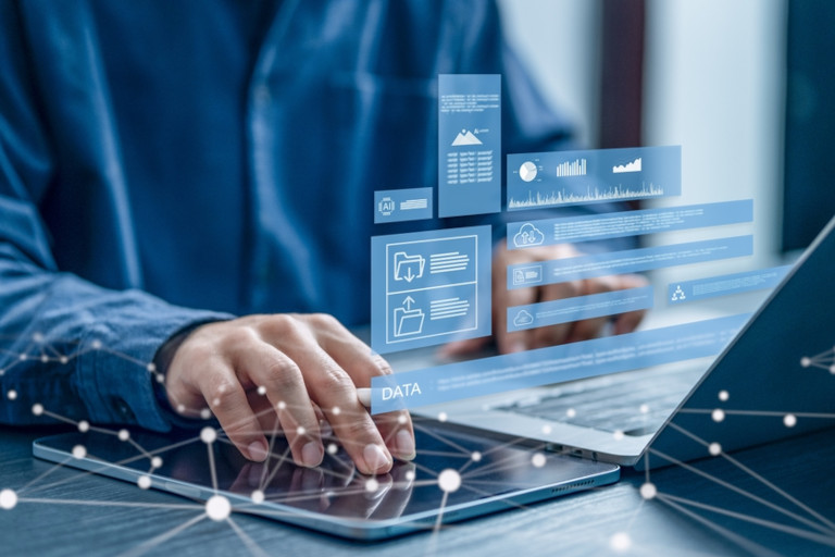 A person works on a laptop while translucent digital data panels and charts float above the screen, symbolizing analytics and information processing.
