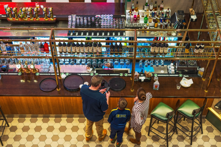 Child standing with his parents as the father reaches into his wallet to pay for drinks at a cocktail bar.