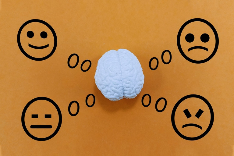A model brain sits at the center of an orange background with illustrated thought bubbles connecting it to four facial expressions—happy, neutral, sad, and angry.