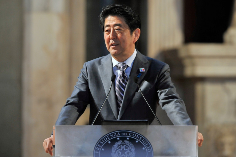 Shinzo Abe giving a speech at a podium outdoors.
