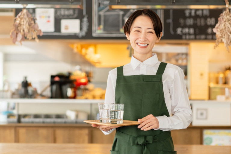 Smiling Japanese server holding a tray with glasses of water in a cafe.