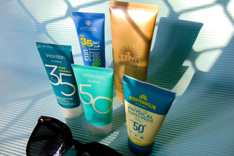 A variety of sunscreen products sitting together with a pair of sunglasses.