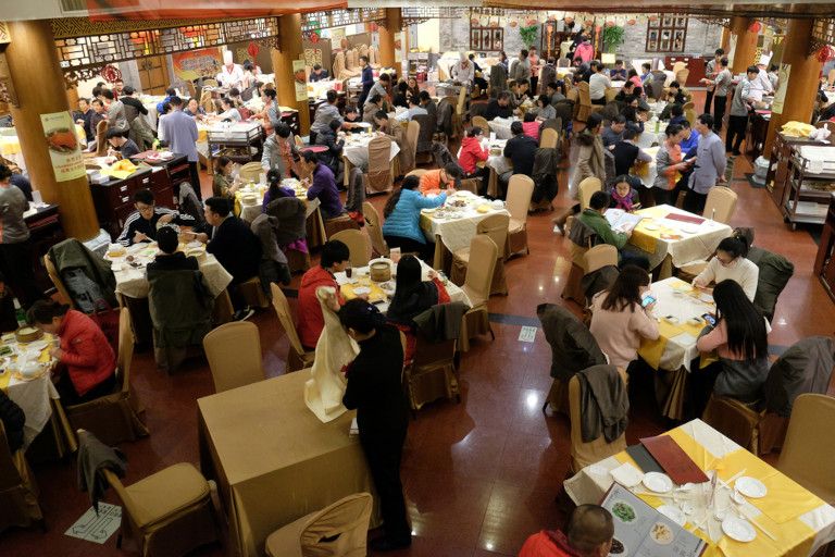 Inside of a Beijing restaurant during a busy period, with lots of customers and workers.
