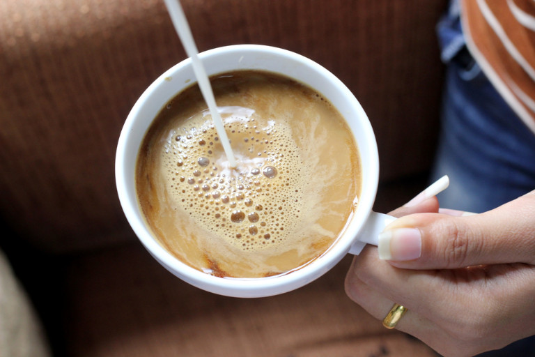 Woman adding cream to her coffee.