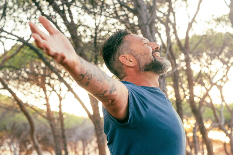 Smiling man outdoors with arms outstretched.