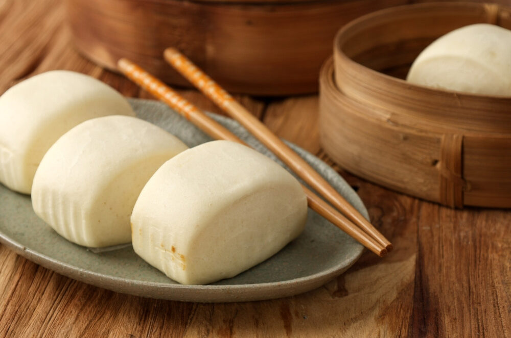Chinese steamed buns, also known as mantou, on a plate with chopsticks next to a steaming basket.