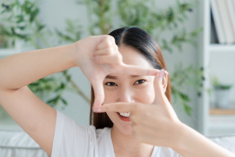 Happy young Asian woman making a frame using her fingers and thumbs to draw attention to her eyes.