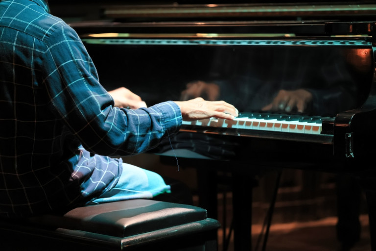 A man plays the piano with his back to the camera.