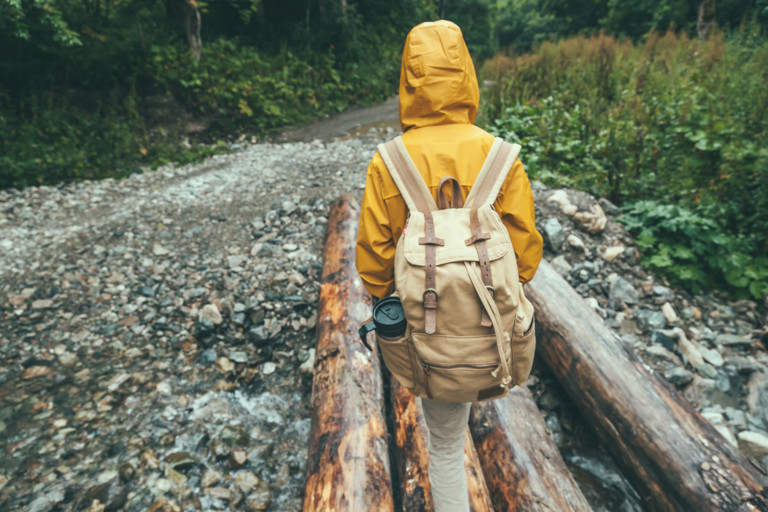 Child wearing a yellow raincoat and a tan backpack while walking outside on a cloudy day.