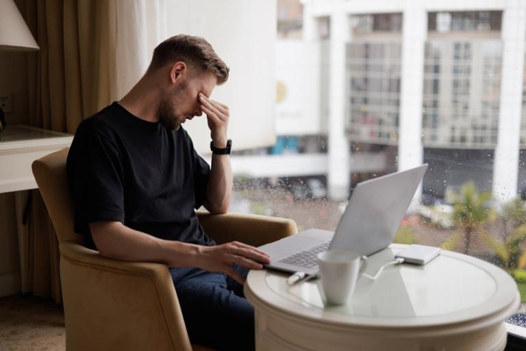Tired laptop user rubbing his eyes.