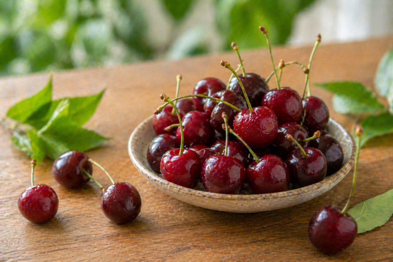 A bowl of cherries sitting on a wooden table. 