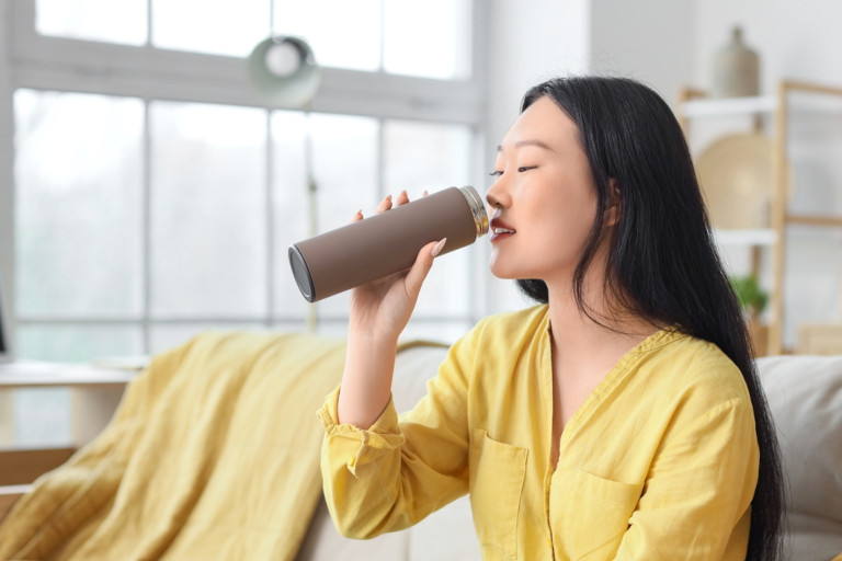 Asian female drinking tea from a thermos.