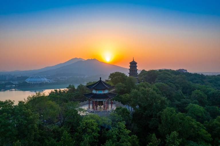 Mount Jiuhua at sunset with a pavilion, pagoda, lake, and tree-covered hills.