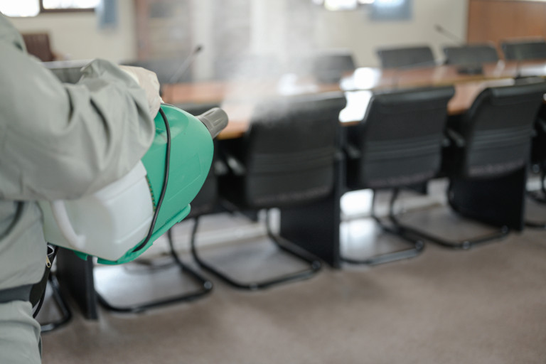 Man in protective clothing spraying disinfectant into an office.