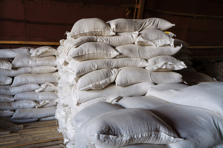 Large cloth bags filled with grain sitting in a warehouse or in the hold of a wooden boat.