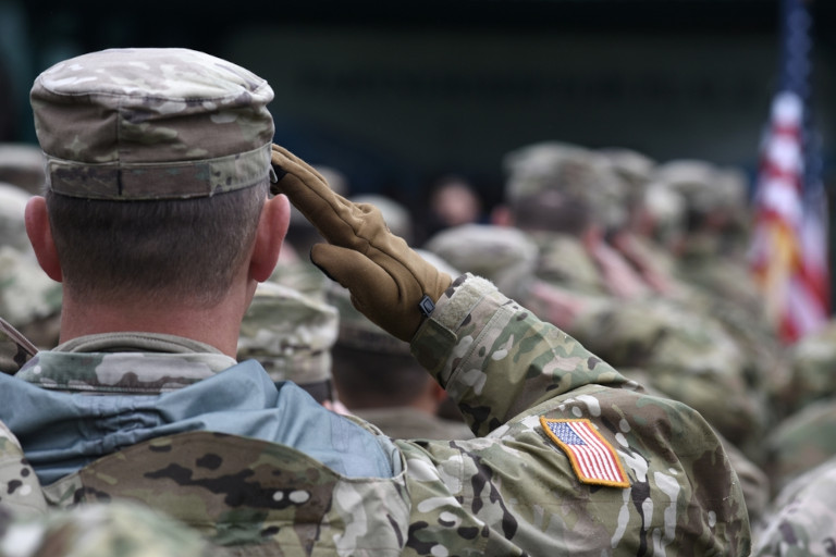 American soldiers lined up in uniform, saluting the U.S. flag.
