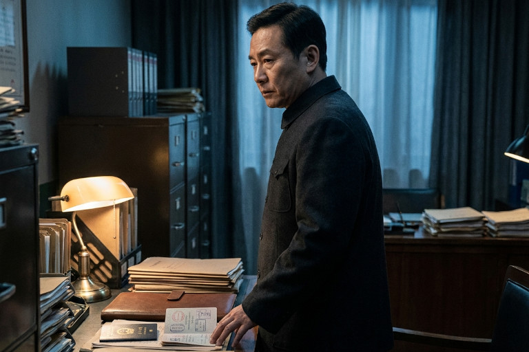 A Chinese intelligence official notices travel documents among folders in a dim office.