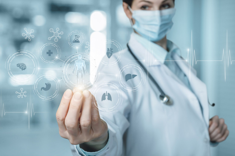 Woman in white coat with a stethoscope and wearing a surgical mask with an overlay of the human body and different organ systems hovering over her hand to symbolize surgery.