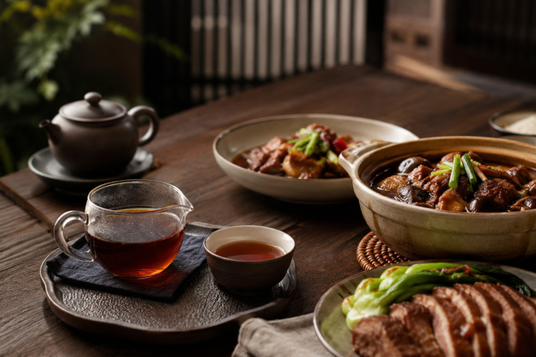 AI-generated image of pu-erh tea served beside a hearty Chinese-style meal on a wooden table.