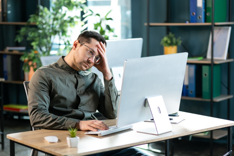 Man sitting at the computer holding his head as though he is tired or experiencing discomfort.