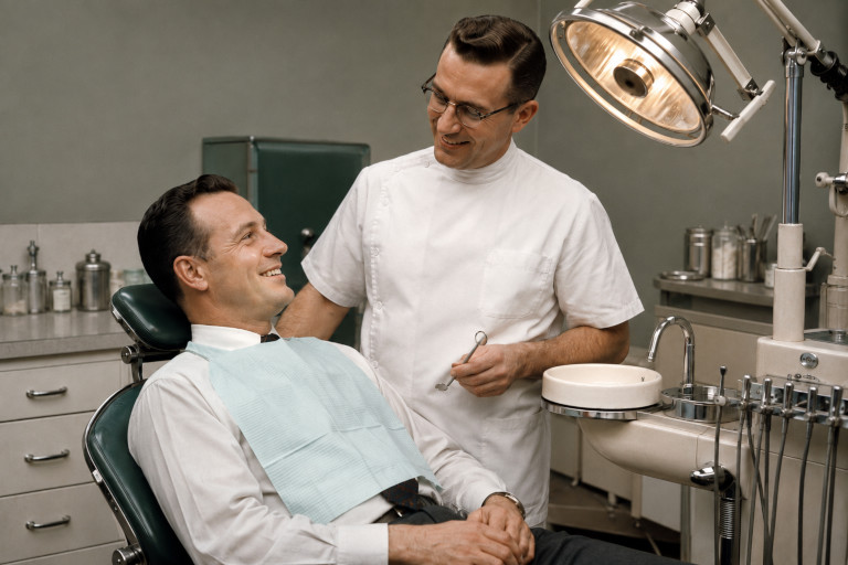 AI-generated image of a smiling patient and dentist in a 1950s dental office with period equipment and an overhead examination light.