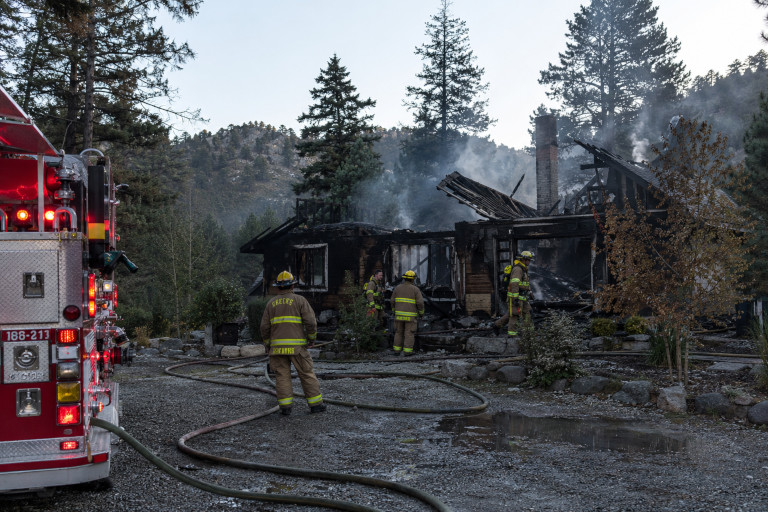 AI-generated image of firefighters working around the charred remains of a mountain cabin as smoke rises after a fire.