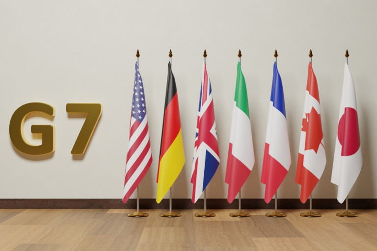 Flags of the 'Group of Seven' nations in a line against a wall next to a sign that says G7.