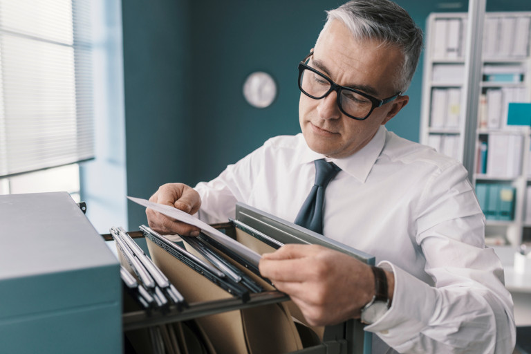 Business man going through files in a filing cabinet.