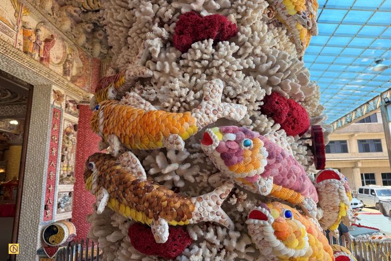 A stunning close-up of the intricately layered shell-art koi swimming up a pillar of white coral at the Coral Shell Temple