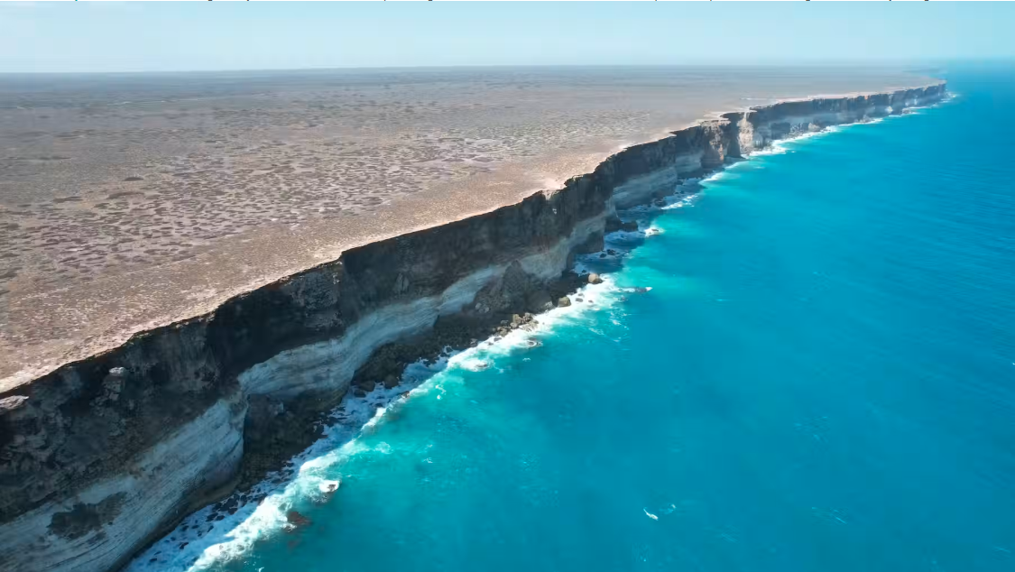 The Bunda Cliffs mark the dramatic edge of the expansive, flat Nullarbor Plain where the arid limestone plains tumble to the Great Australian Bight. Distinct limestone layers are visible in the cliffs, with the Nullarbor Limestone overlying the white, chalkier layer known as the Wilson Bluff Limestone.