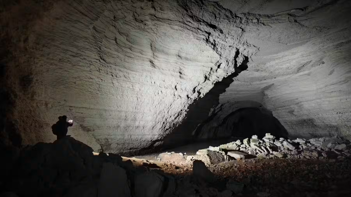The dramatic Abrakurrie Cave system beneath the Nullarbor Plain. The photo shows the scale, dwarfing the team member, as well as evidence of cave-collapse processes (a pile of boulders and rubble in view) that allow the cave to move upward through the overlying rocks to the surface over time.
