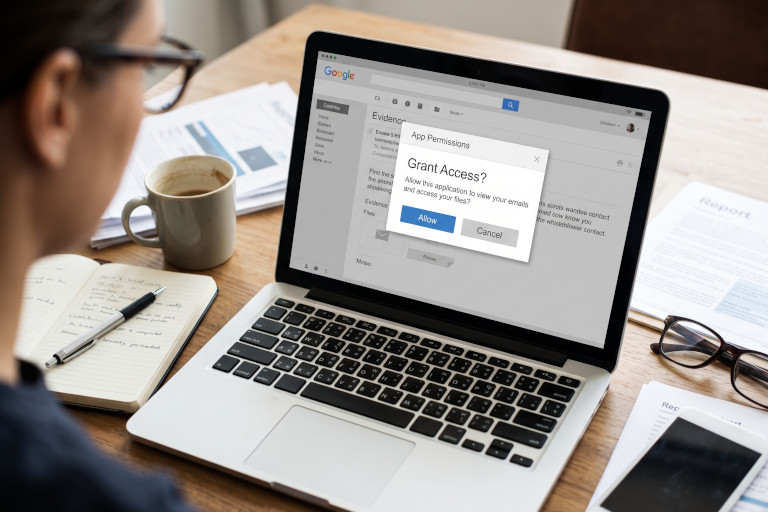 AI-generated image of a laptop displaying an account-access request while a user reviews documents at a desk.
